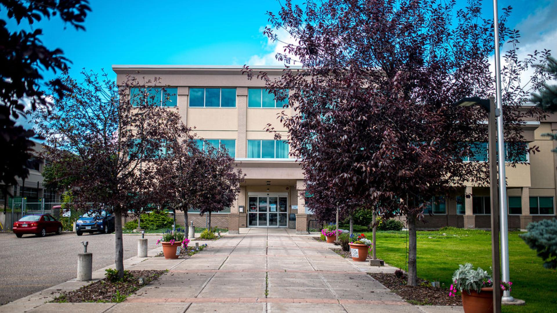 beige building with a walkway in front lined with trees