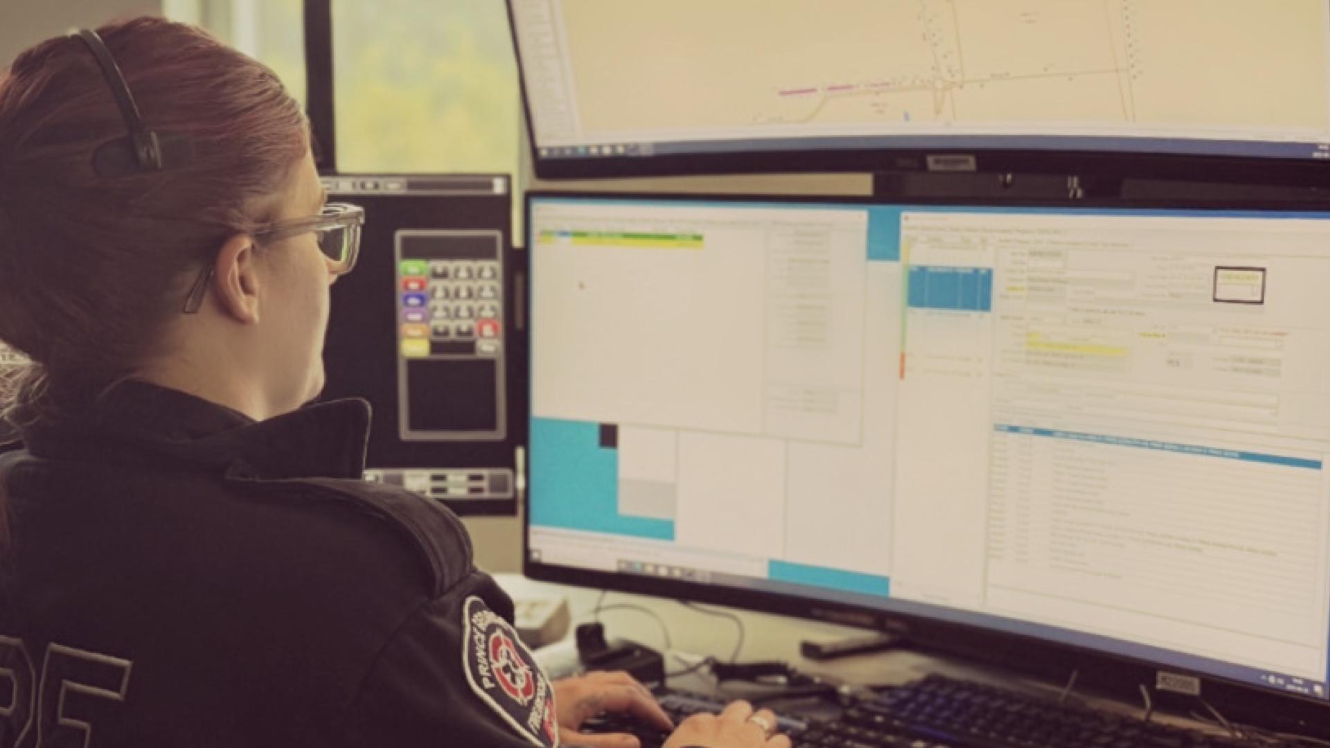 woman in dark clothing sitting at computer with multiple monitors