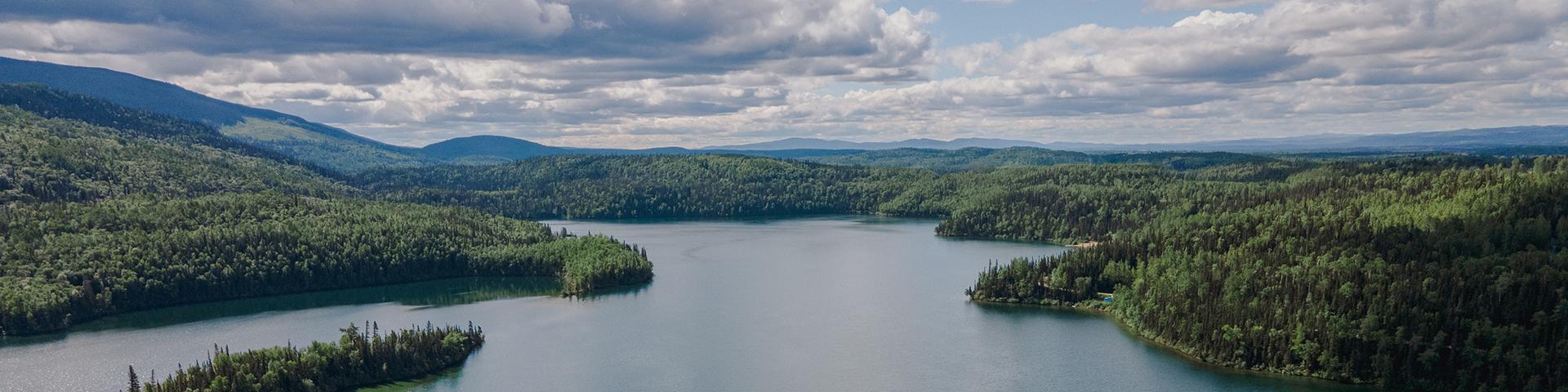 lake with green water surrounded by evergreen trees and rolling mountains