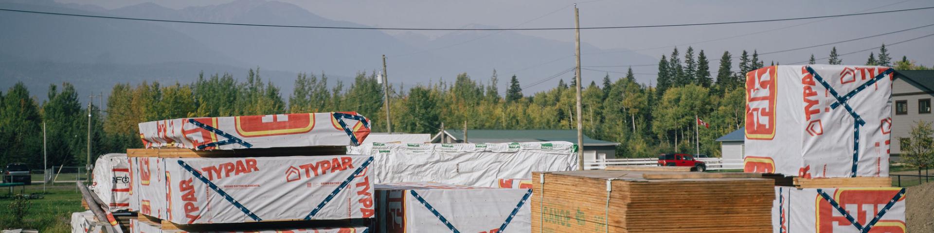 pallets of lumber on the ground with trees and mountains in the background