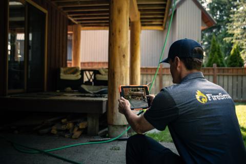 man in a dark shirt and hat taking a photo of a home exterior